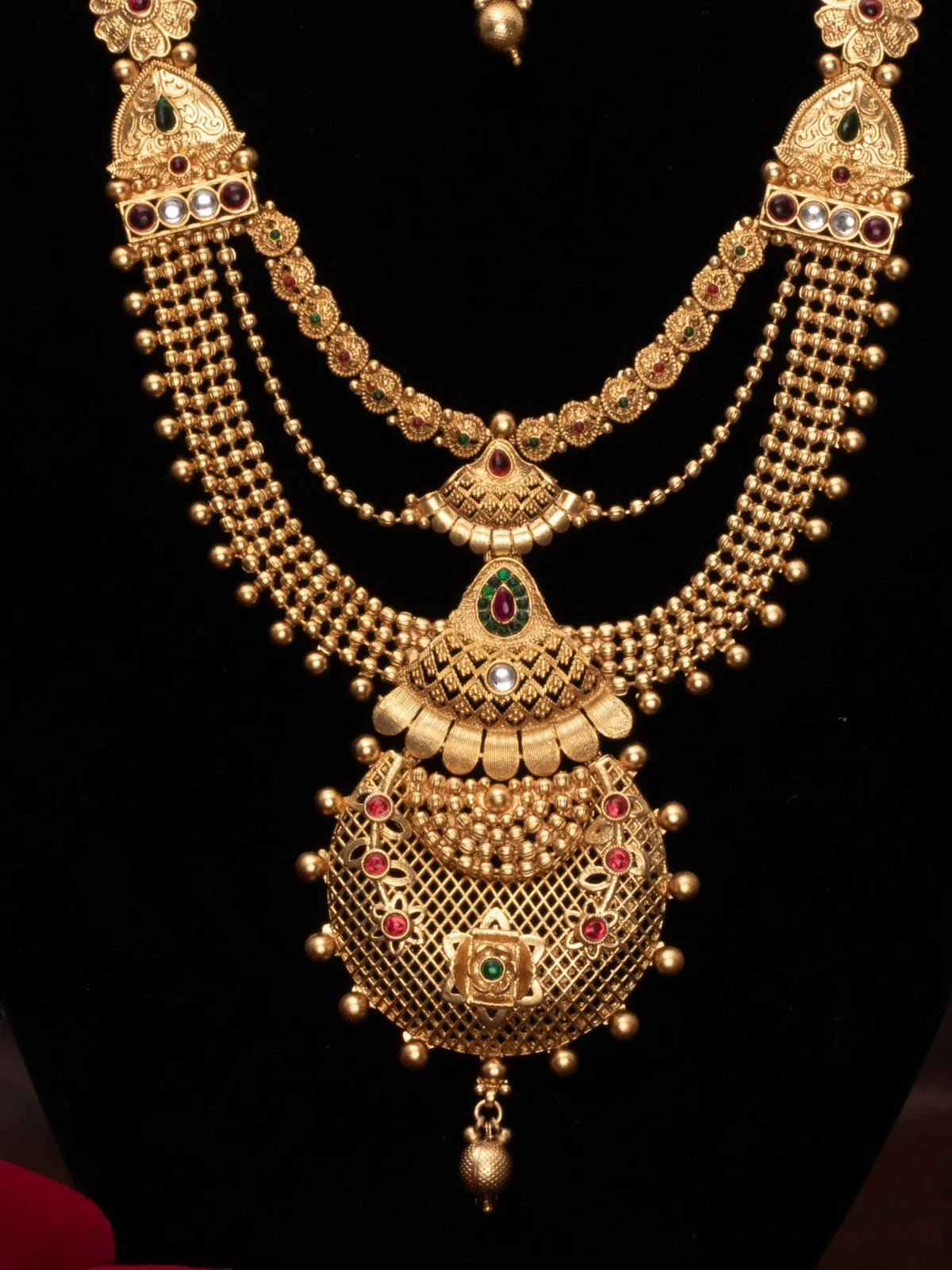 Tarani closeup of gold plated bridal necklace set with red and green stone detailing for festive occasions