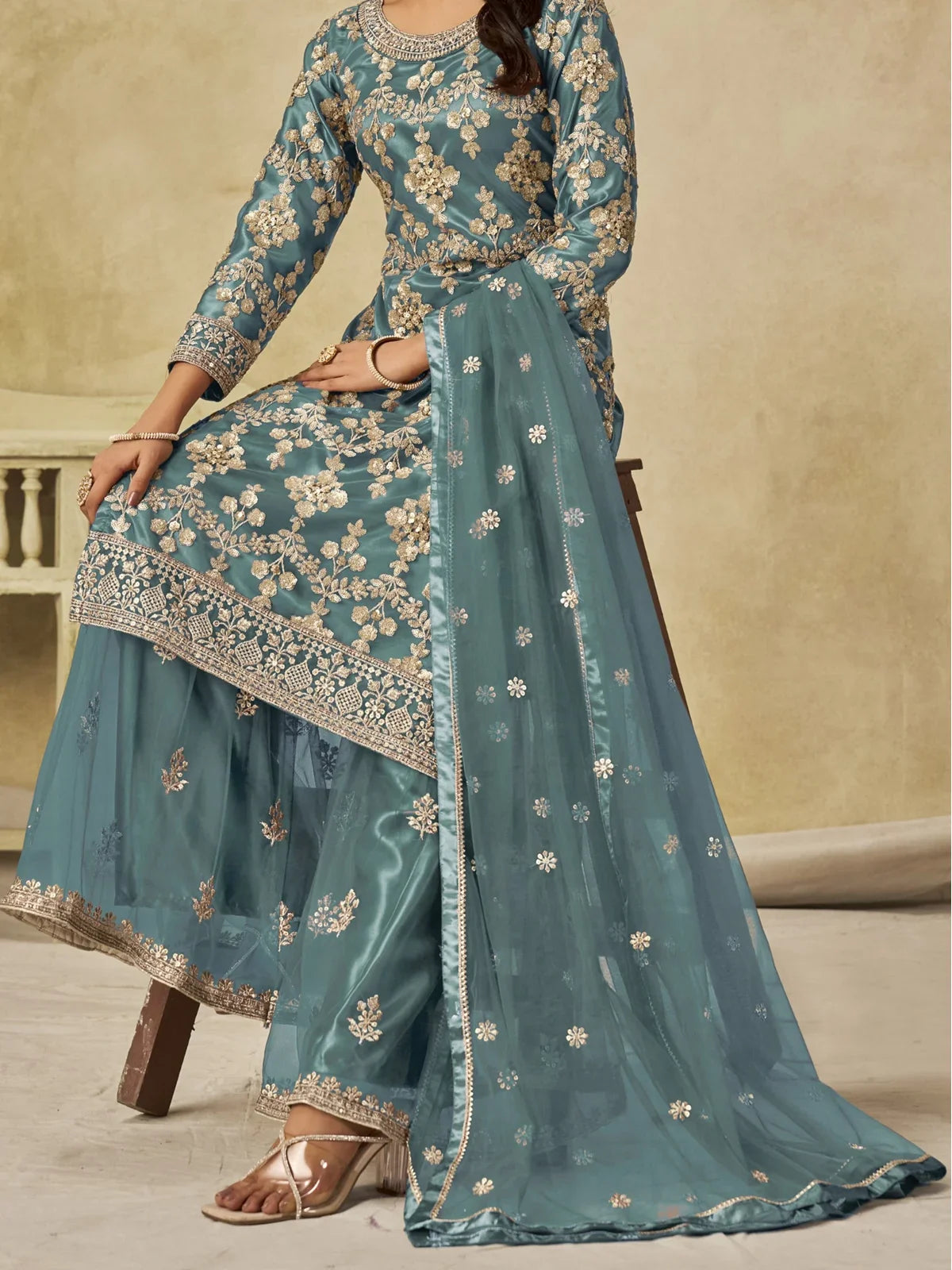 Tarani teal net sharara suit sitting pose highlighting embroidered palazzo and dupatta