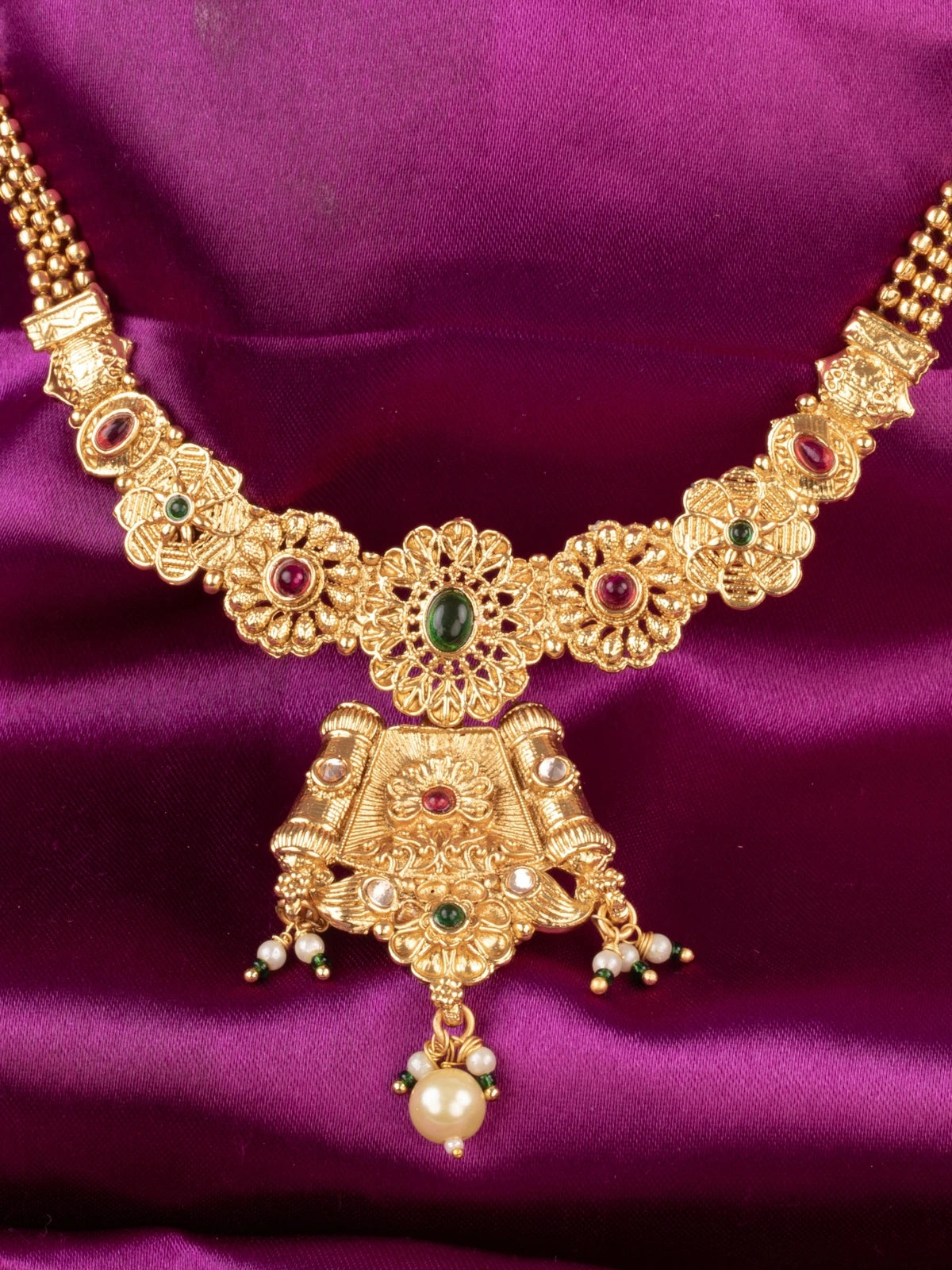 Tarani closeup gold plated necklace with green and red stone studded detailing for weddings