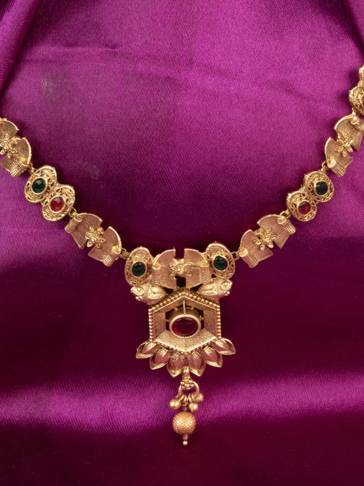 Tarani closeup view of gold necklace set with antique red and green stone detailing