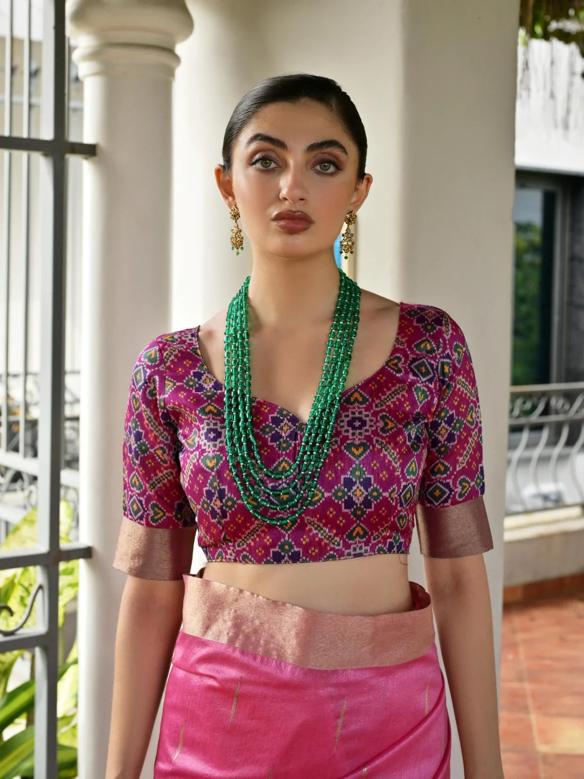 Tarani pink silk saree close upper body showcasing deep neckline blouse in ikkat weave and green jewelry