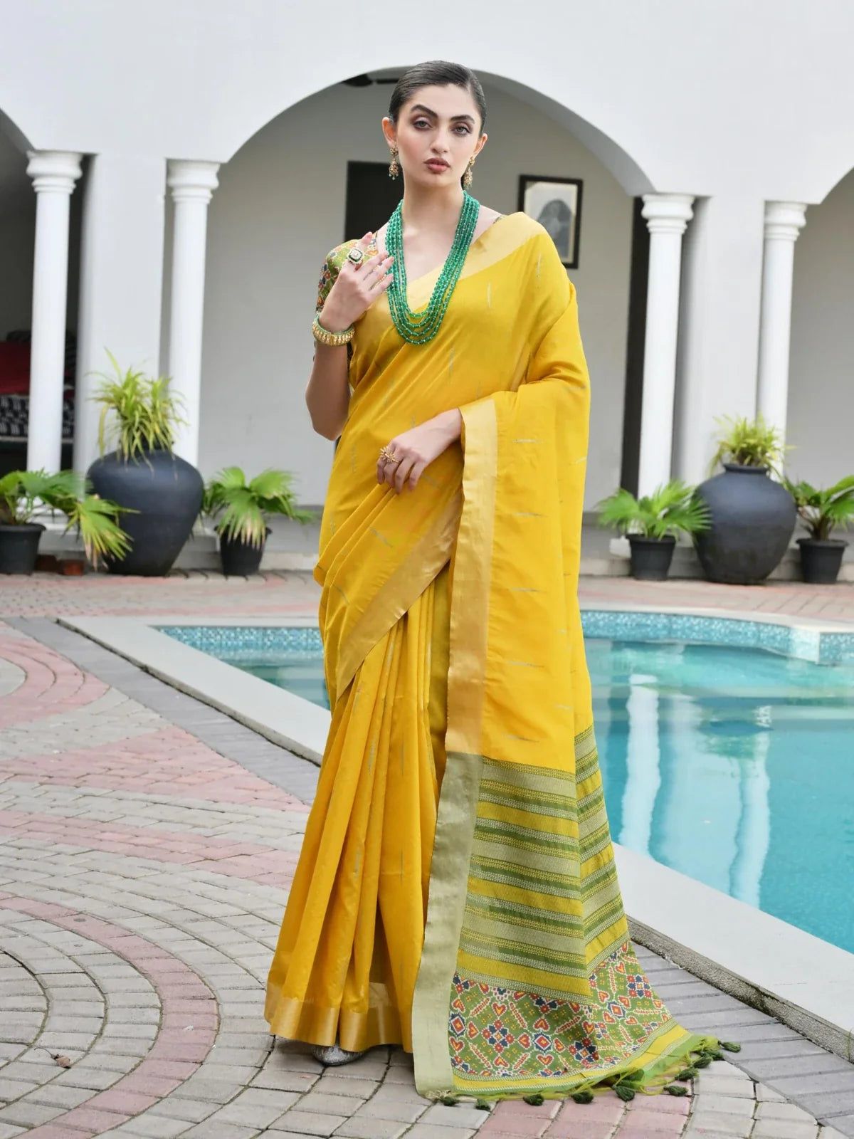 Tarani yellow silk saree full view with traditional border and ikkat pallu near poolside