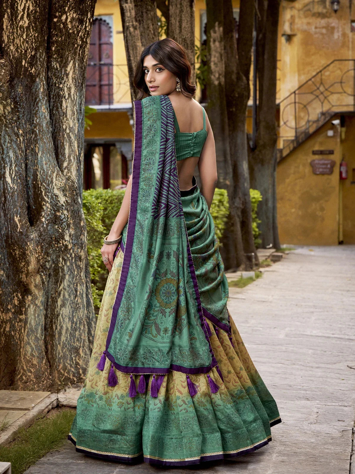 Tarani back view of printed green Vichitra silk lehenga with dupatta tassels and elegant pleats